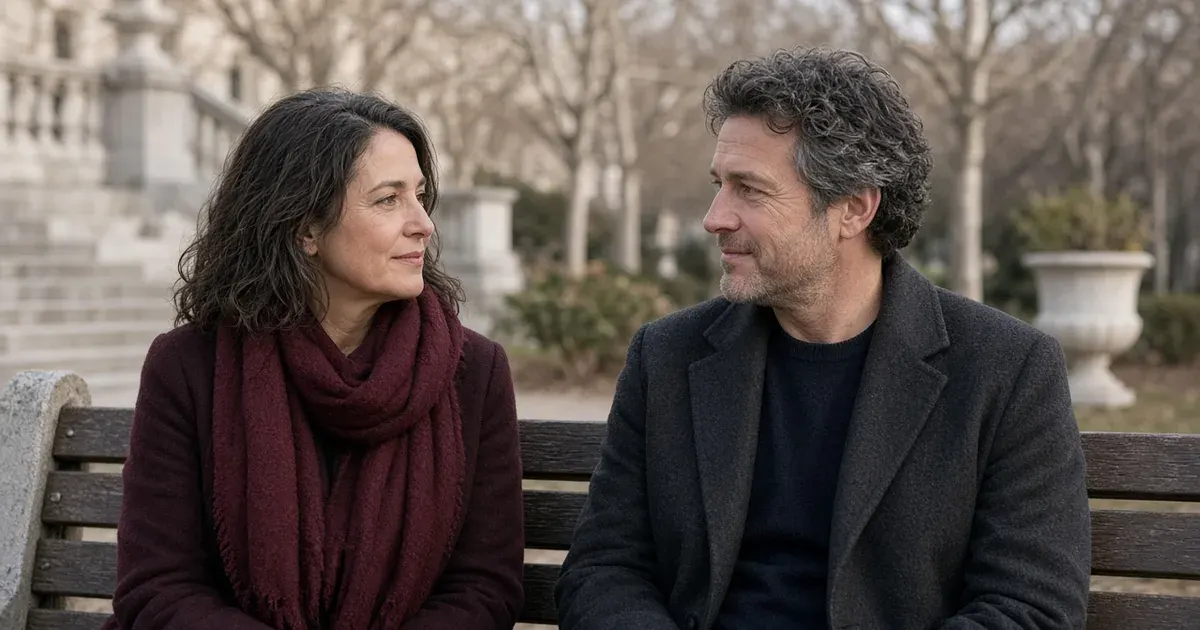 A woman and a man in their forties in a frank, warm conversation on a park bench, she in a burgundy scarf.